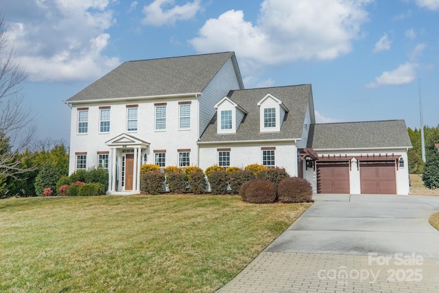 colonial inspired home featuring a garage, concrete driveway, a front lawn, and roof with shingles