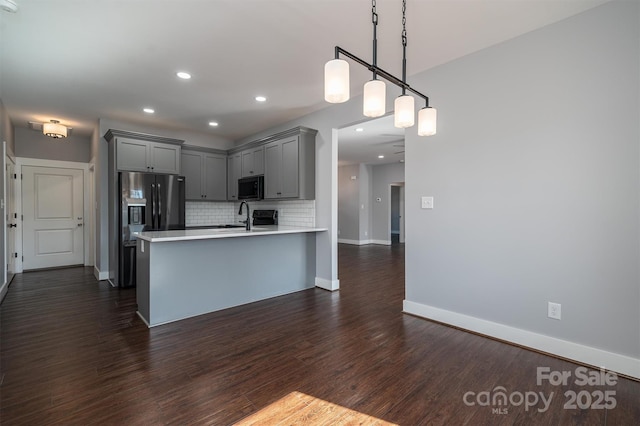 kitchen featuring sink, decorative light fixtures, dark wood-type flooring, kitchen peninsula, and decorative backsplash