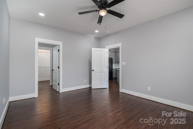 unfurnished bedroom with a closet, black refrigerator, ceiling fan, a walk in closet, and dark hardwood / wood-style floors