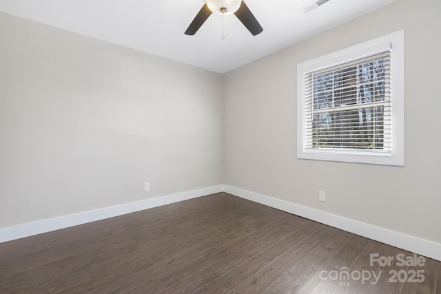 spare room with dark wood-type flooring, a ceiling fan, visible vents, and baseboards