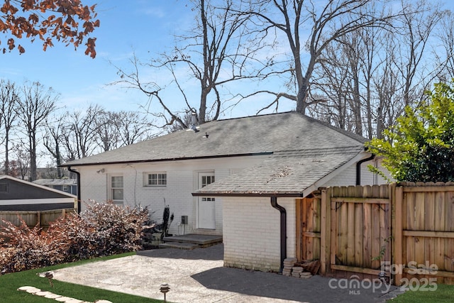 rear view of property featuring a shingled roof, brick siding, and fence