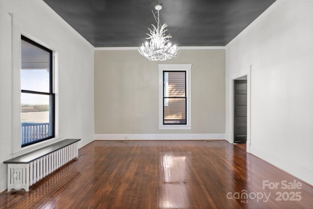 empty room with dark wood-type flooring, a chandelier, crown molding, and radiator heating unit