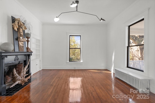 living room featuring built in shelves, radiator heating unit, a tile fireplace, crown molding, and dark hardwood / wood-style flooring