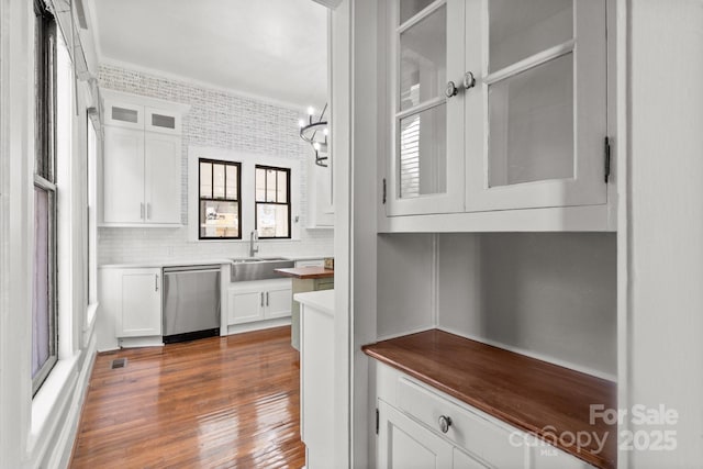 interior space featuring stainless steel dishwasher, hardwood / wood-style floors, ornamental molding, sink, and white cabinetry