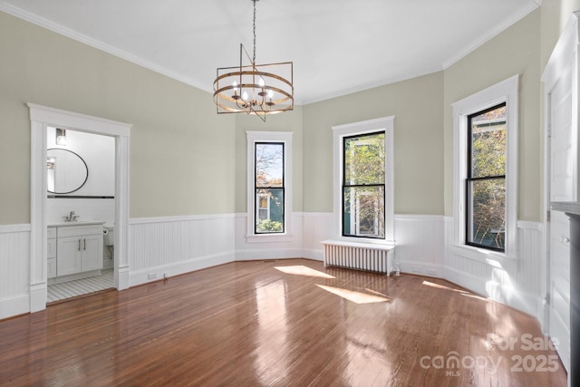 unfurnished dining area featuring ornamental molding, radiator, hardwood / wood-style flooring, and a notable chandelier