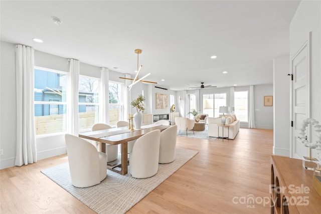 dining space with baseboards, a glass covered fireplace, light wood-style floors, a chandelier, and recessed lighting