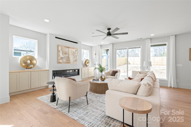 living area with light wood finished floors, recessed lighting, visible vents, a glass covered fireplace, and baseboards