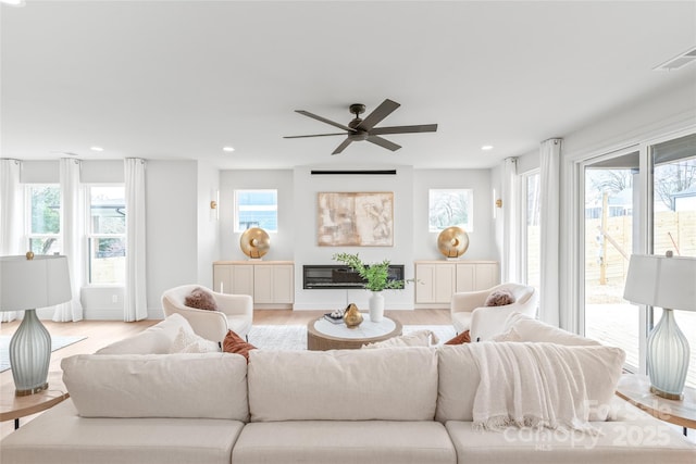 living area with baseboards, visible vents, a glass covered fireplace, light wood-style floors, and recessed lighting