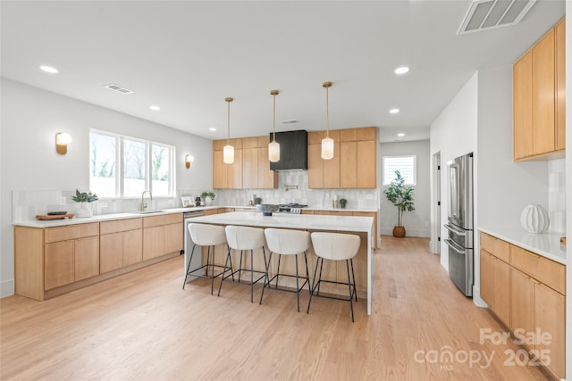 kitchen with a breakfast bar area, light brown cabinets, light wood-style flooring, visible vents, and appliances with stainless steel finishes