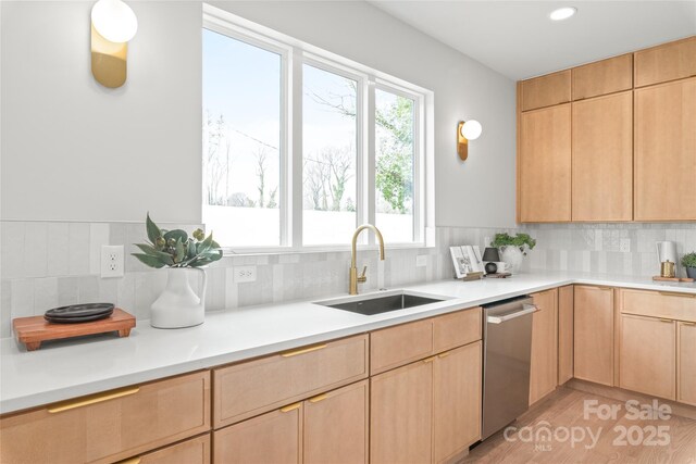 kitchen featuring light countertops, decorative backsplash, light brown cabinets, a sink, and dishwasher