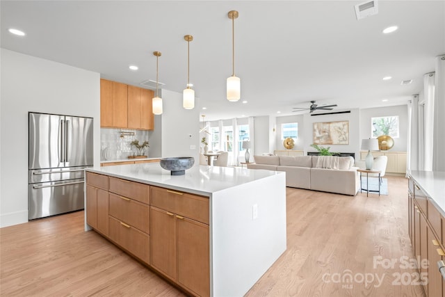 kitchen with light wood-style flooring, a kitchen island, visible vents, light countertops, and freestanding refrigerator