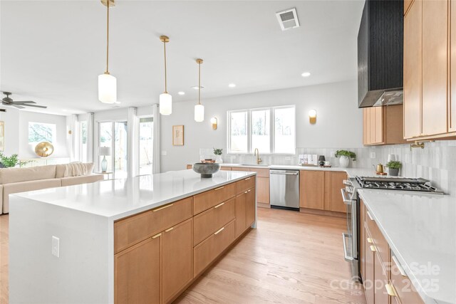 kitchen with wall chimney range hood, appliances with stainless steel finishes, a sink, and a wealth of natural light