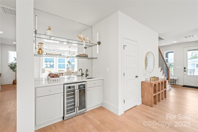 bar featuring wine cooler, indoor wet bar, light wood finished floors, visible vents, and stairway