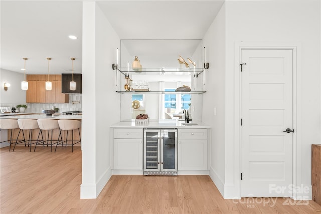 bar featuring wine cooler, indoor bar, a sink, backsplash, and light wood finished floors