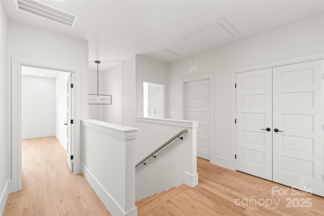 hall featuring light wood-style flooring, visible vents, attic access, and an upstairs landing