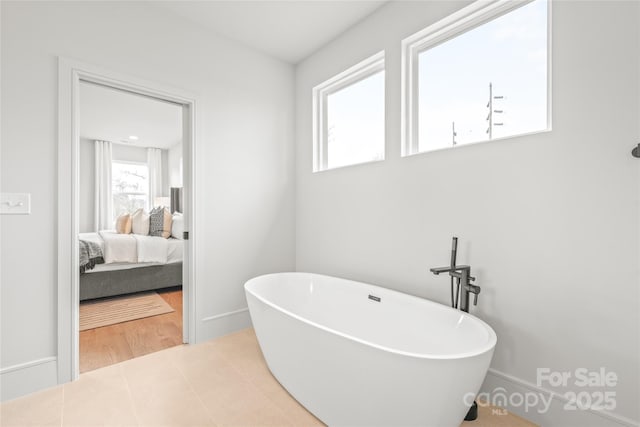 ensuite bathroom featuring tile patterned floors, a soaking tub, baseboards, and ensuite bathroom