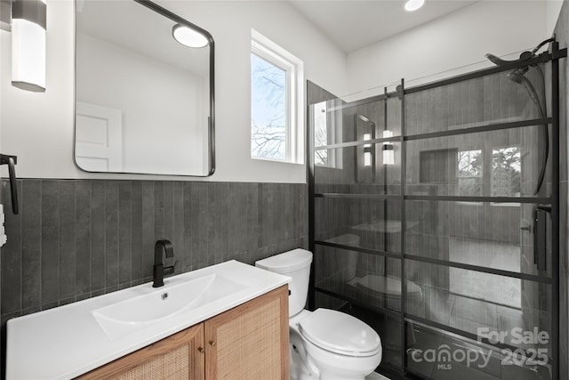 full bath featuring a wainscoted wall, tile walls, toilet, a tile shower, and vanity