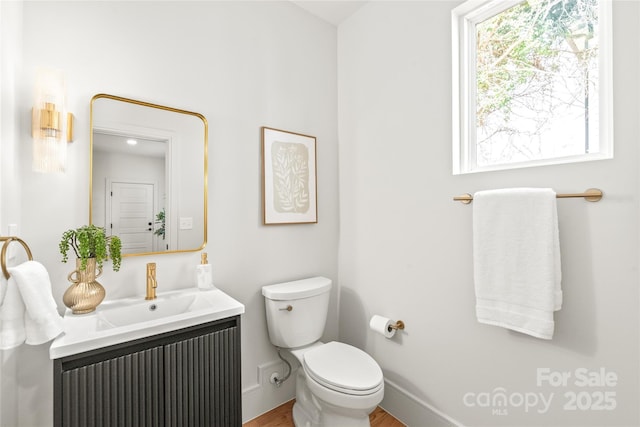 half bathroom with toilet, baseboards, and vanity