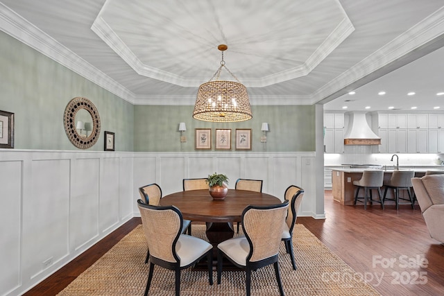 dining area with a chandelier, a decorative wall, dark wood-style floors, a tray ceiling, and crown molding