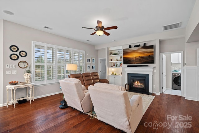 living room with washer / clothes dryer, visible vents, a fireplace with flush hearth, a ceiling fan, and wood finished floors