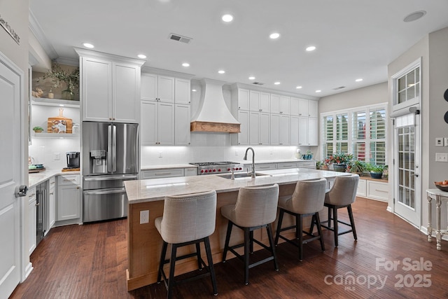 kitchen with stainless steel fridge, visible vents, custom range hood, light stone counters, and a sink