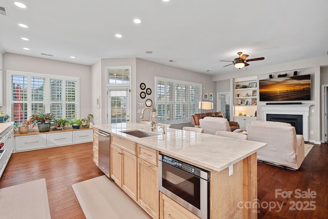 kitchen featuring dark wood finished floors, a fireplace, a sink, built in microwave, and dishwasher