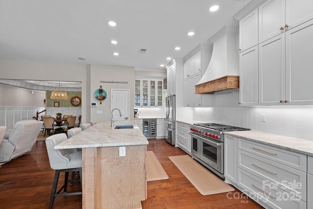 kitchen with dark wood-style floors, custom exhaust hood, appliances with stainless steel finishes, a sink, and a kitchen breakfast bar