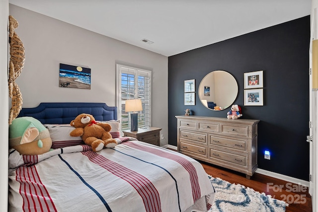 bedroom with baseboards, visible vents, and wood finished floors