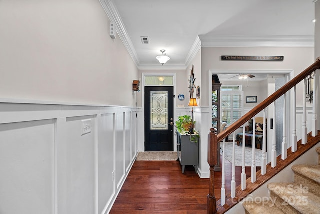 foyer entrance with dark wood-style flooring, a wainscoted wall, visible vents, ornamental molding, and stairs