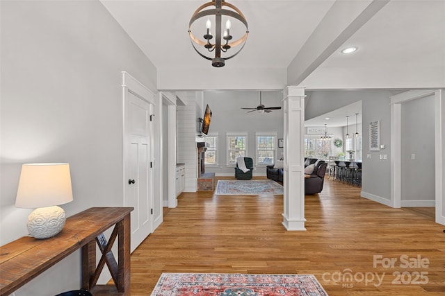 entryway featuring light wood-type flooring, ornate columns, and ceiling fan with notable chandelier