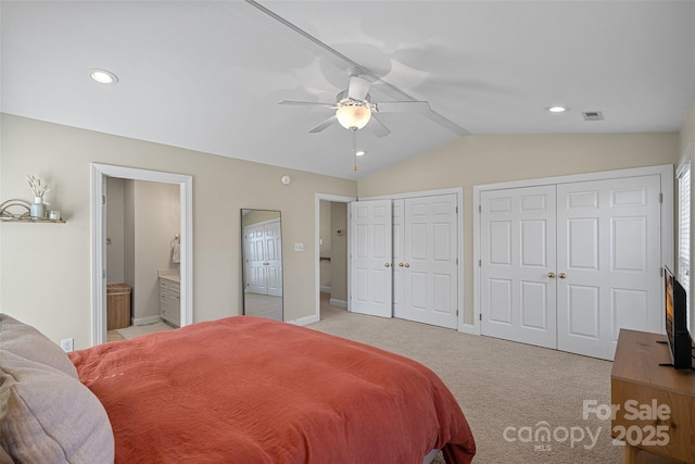 bedroom featuring lofted ceiling, light colored carpet, two closets, ensuite bath, and ceiling fan