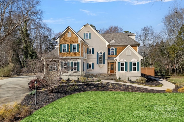 traditional home featuring a shingled roof, driveway, a front lawn, and stucco siding