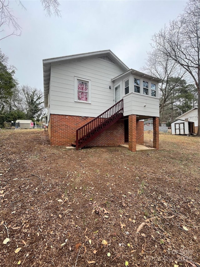 rear view of house featuring an outbuilding, brick siding, stairway, and a shed