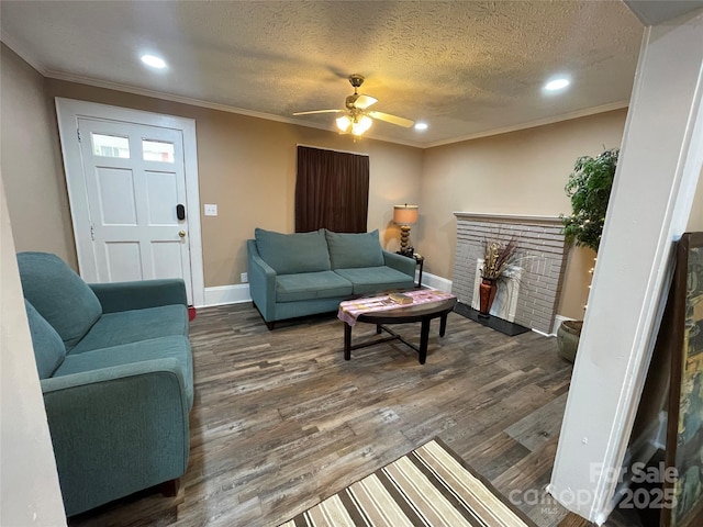 living room with dark wood-type flooring, a brick fireplace, ornamental molding, and a textured ceiling