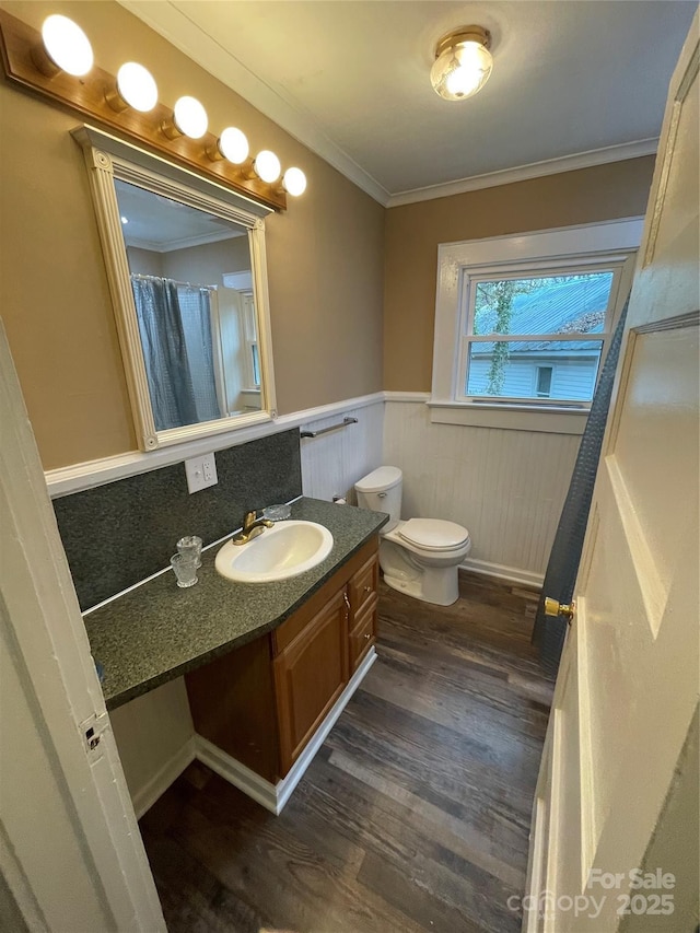 full bath featuring a wainscoted wall, crown molding, toilet, vanity, and wood finished floors