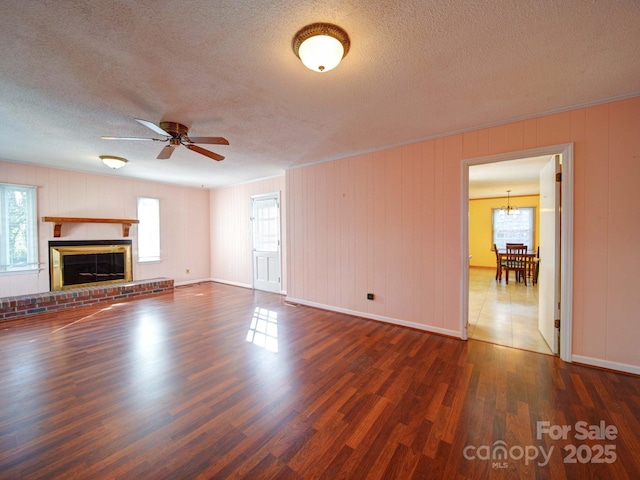 unfurnished living room featuring ceiling fan with notable chandelier, dark hardwood / wood-style flooring, a textured ceiling, and a fireplace