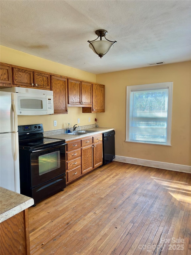 kitchen with light countertops, brown cabinets, a sink, and black appliances