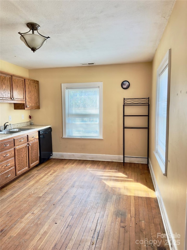 kitchen featuring black dishwasher, light countertops, a sink, and brown cabinets