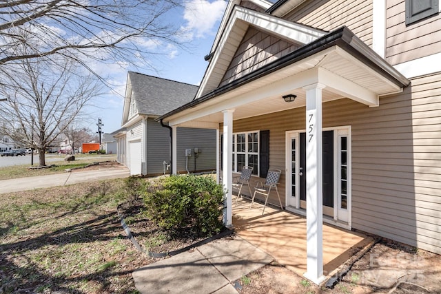 view of exterior entry featuring a porch, concrete driveway, a garage, and a shingled roof