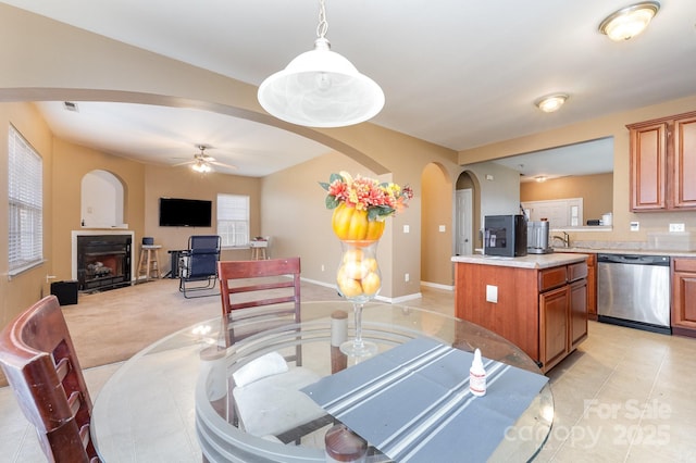 dining room featuring arched walkways, light tile patterned flooring, a fireplace, baseboards, and ceiling fan