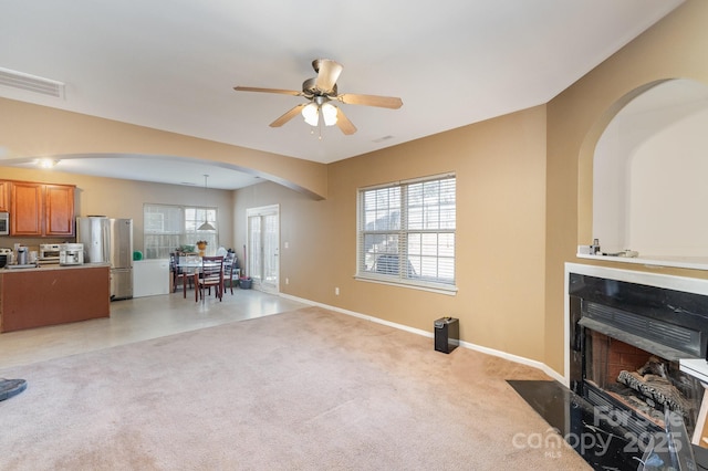 living room featuring light carpet, a fireplace with flush hearth, a ceiling fan, arched walkways, and baseboards