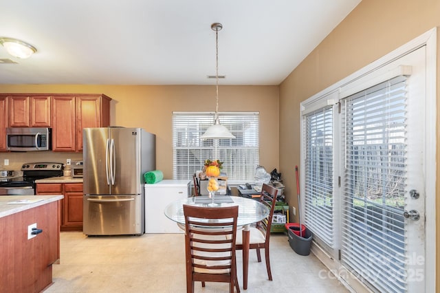 kitchen featuring stainless steel appliances, brown cabinetry, light countertops, light floors, and hanging light fixtures