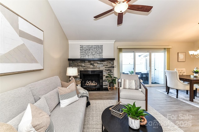 living room featuring a stone fireplace, ceiling fan with notable chandelier, and wood finished floors