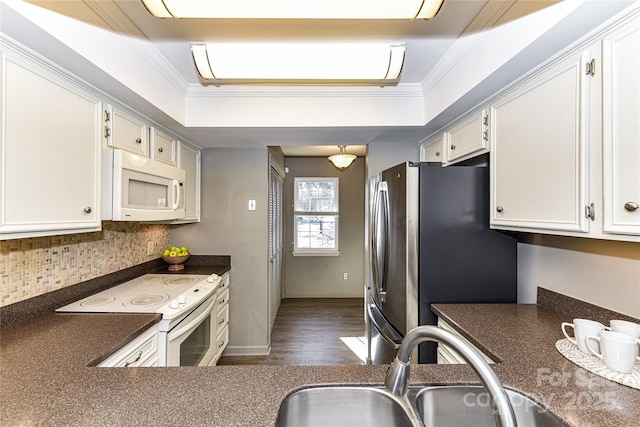 kitchen with white appliances, ornamental molding, dark countertops, and a sink