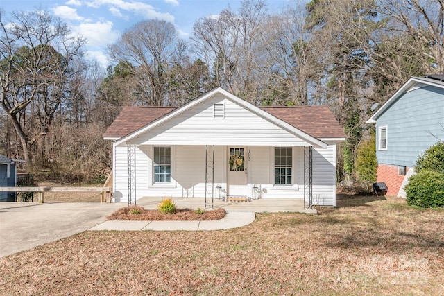 bungalow-style house featuring covered porch, concrete driveway, a front lawn, and roof with shingles