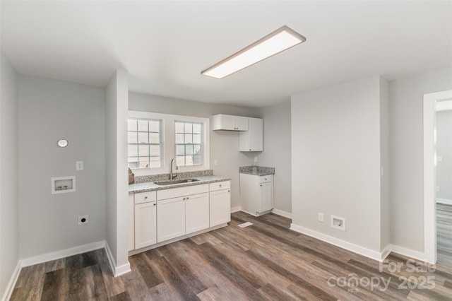 kitchen with dark wood-style floors, a sink, white cabinets, and light stone countertops