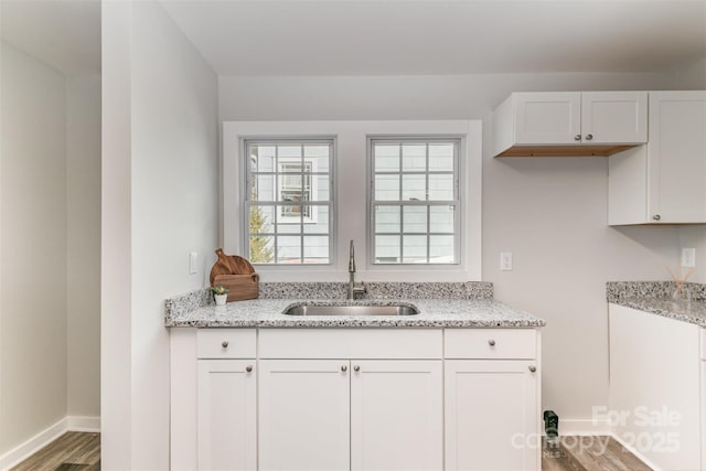 kitchen with baseboards, light stone counters, wood finished floors, white cabinetry, and a sink