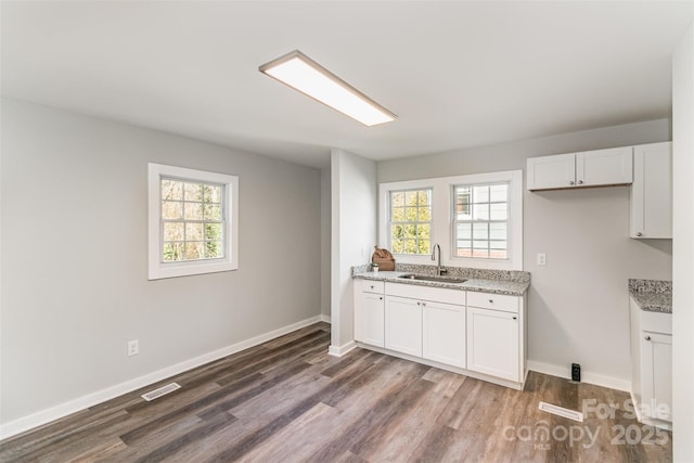 kitchen with dark wood-style floors, white cabinetry, a sink, and light stone countertops