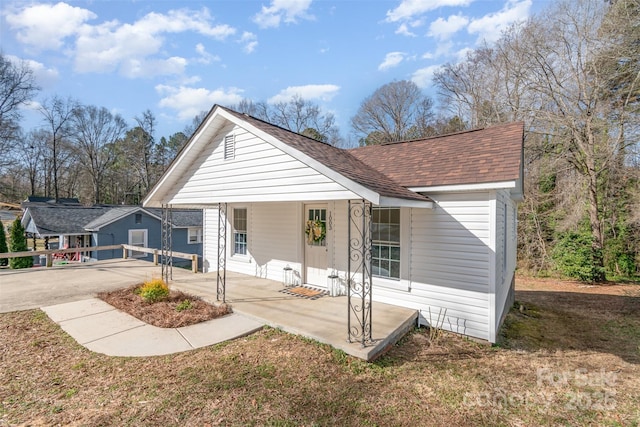 view of front of house with roof with shingles, a patio, and a front lawn