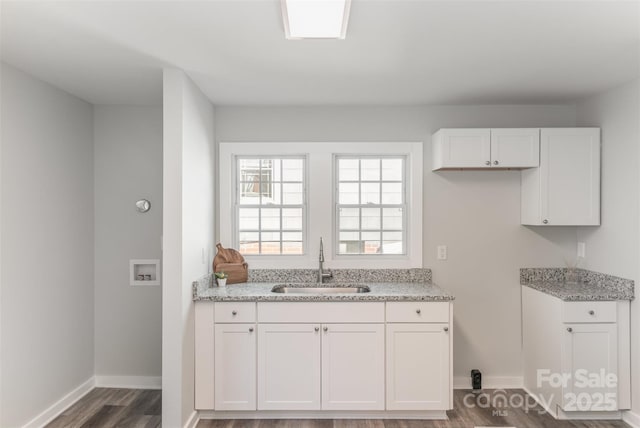 kitchen featuring dark wood-type flooring, a sink, baseboards, white cabinets, and light stone countertops